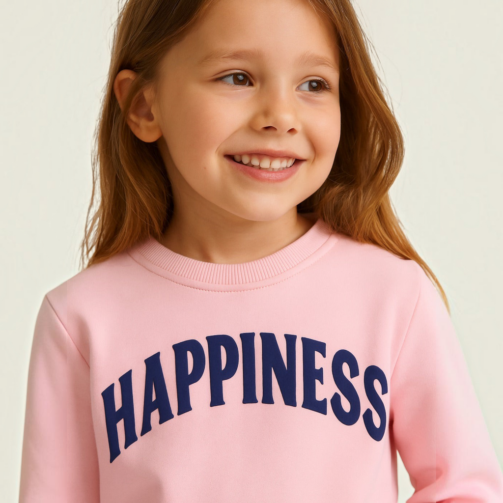 Young girl smiling while wearing a light pink victor and jane EURA sweatshirt with navy blue HAPPINESS text